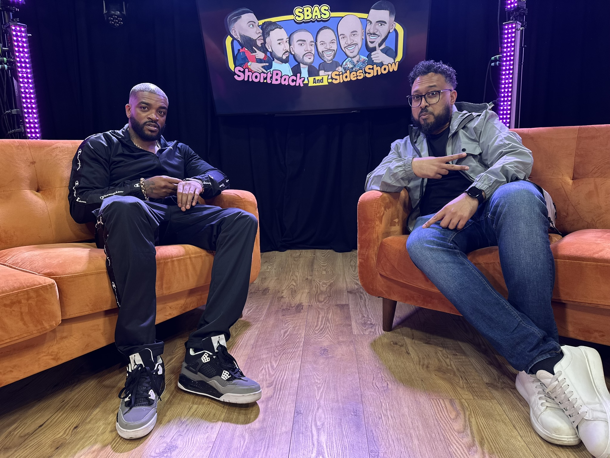 Two podcast presenters recording on the orange sofa set at Podcast Studio Leicester