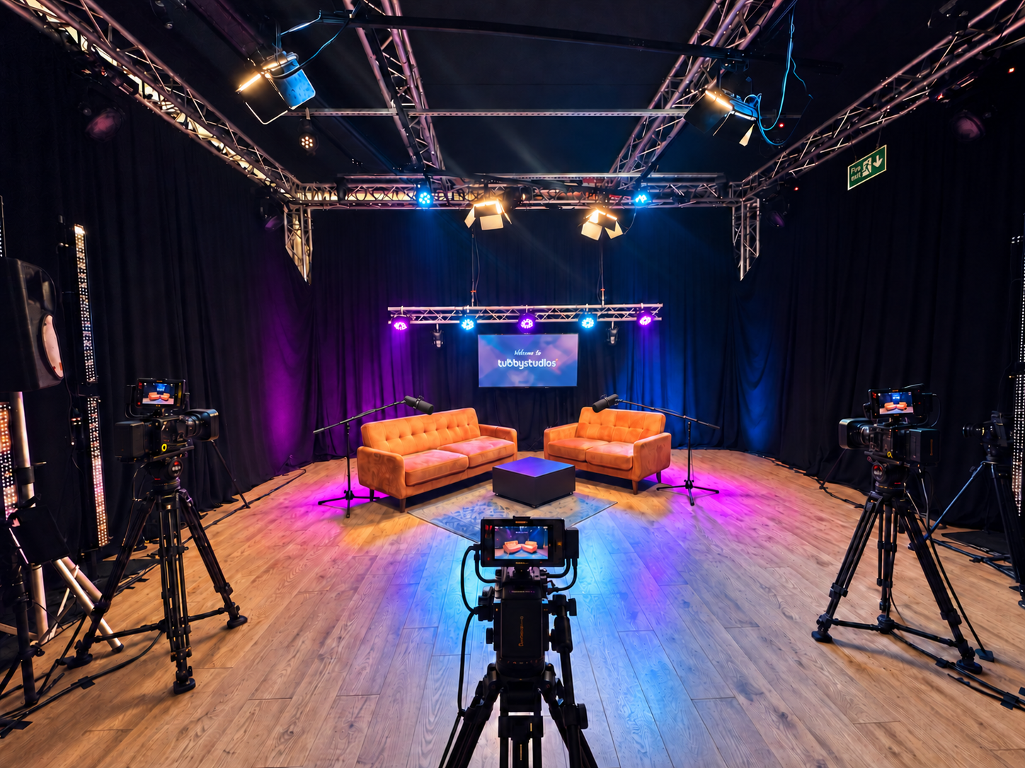 Wide view of Podcast Studio Leicester showing the orange sofa set, four cameras, lighting rig and branded screen